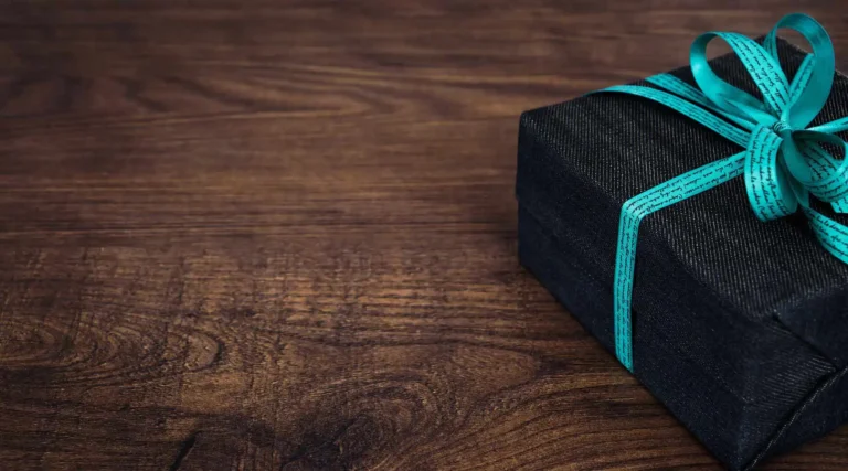 Nell'immagine, il primo piano su un pacco regalo con un fiocco azzurro poggiato su un tavolo in legno.
